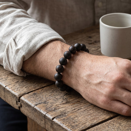 Black Gold hand-rolled incense bead bracelet worn on a man's wrist at a wooden table