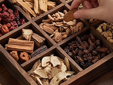 Whole botanicals laid out in a compartmented wooden tray, picked over by hand