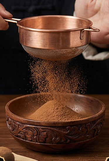 Powder sifted through a copper sieve into a carved wooden bowl